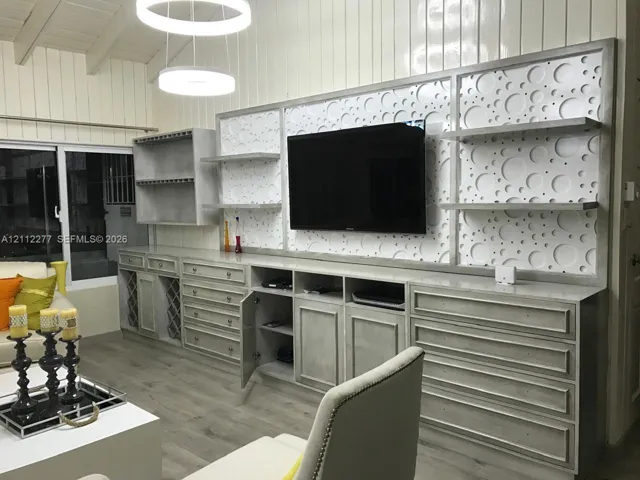 Custom floor-to-ceiling built-in cabinetry featuring multi-drawer storage, open display shelving, a designated wine rack, and a decorative circular-patterned back panel with integrated screen mounting