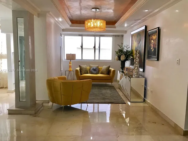 Interior room featuring polished stone flooring, a recessed tray ceiling with metallic finish, decorative crown molding, a central drum pendant light, and a column with an inset mirror panel