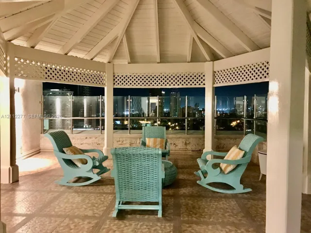 Covered gazebo featuring a vaulted ceiling with exposed rafters, white lattice trim, tile flooring, and a glass-paneled railing