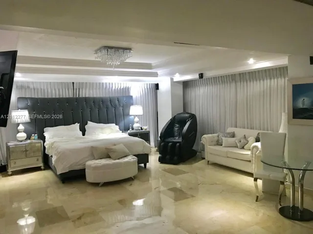 Spacious room featuring polished stone flooring, recessed tray ceiling, tiered crystal chandelier, and floor-to-ceiling window drapery