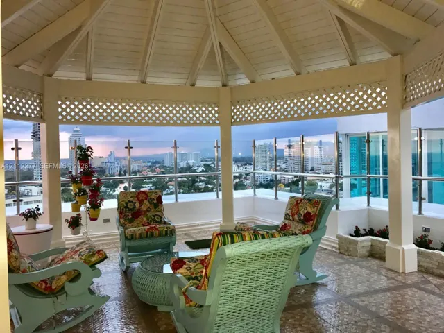 Covered terrace featuring a vaulted wood-beam ceiling, decorative lattice trim, tiled flooring, and a glass-paneled metal railing