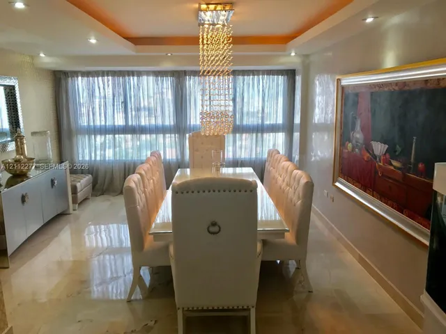 Dining area featuring polished stone flooring, recessed tray ceiling, multi-level crystal pendant chandelier, and built-in white lacquer sideboard