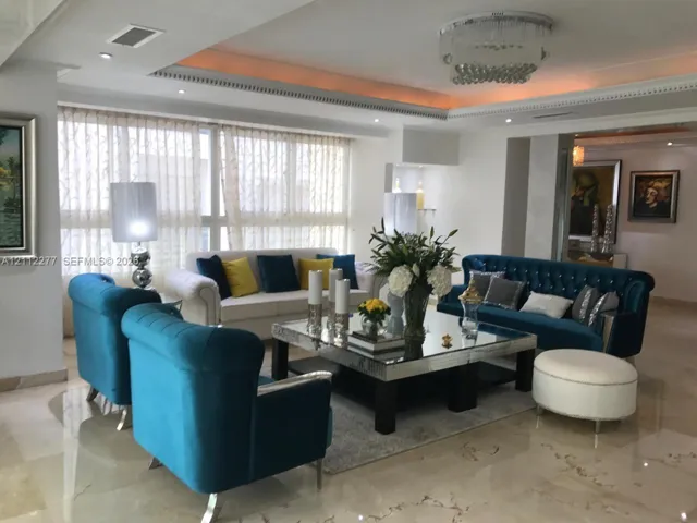 Spacious living area featuring polished stone flooring, recessed lighting, crown molding, a decorative crystal-style ceiling fixture, and floor-to-ceiling windows with integrated drapery