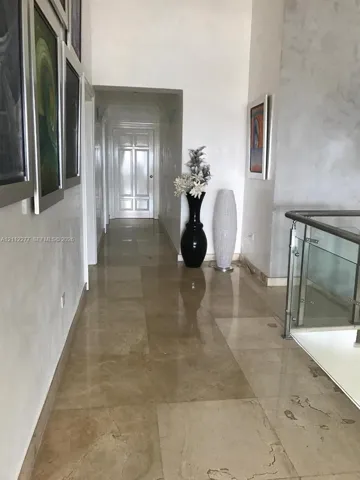 Hallway featuring high-gloss large-format stone flooring, textured wall finishes, and a glass-paneled railing with a metal handrail
