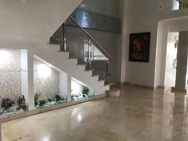 Staircase featuring a glass railing and metallic handrail, complemented by integrated under-stair plant beds with stone accents and three-dimensional textured wall tiles, finished with polished stone flooring