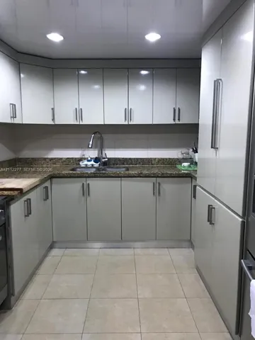 Kitchen featuring high-gloss cabinetry with bar pulls, stone-finish countertops, stainless steel dual-basin sink, recessed ceiling lighting, and tile flooring