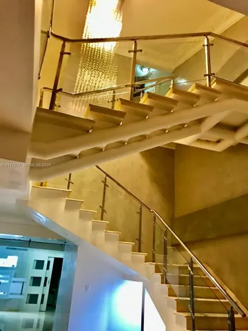 Staircase featuring open-riser treads, a glass-panel balustrade with metal hardware, a handrail, and a tiered crystal chandelier