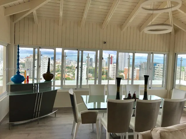 Vaulted ceilings with exposed beams, continuous panoramic windows, wood-finish flooring, and circular pendant lighting