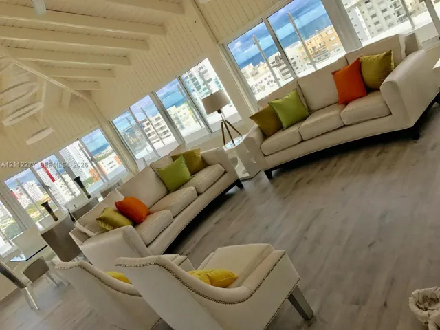 Vaulted ceiling with exposed white-finished beams, expansive floor-to-ceiling windows, wood-finish flooring, and minimalist ring-style pendant lighting