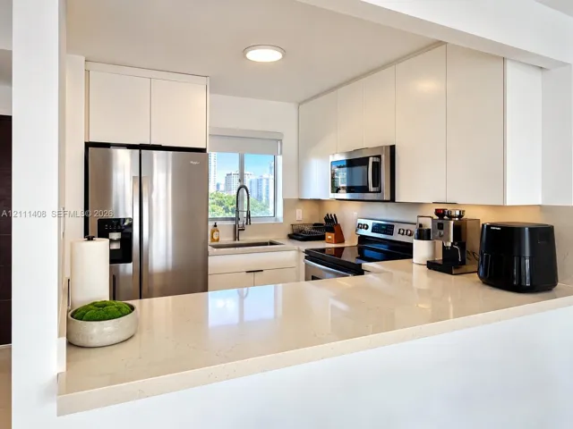 Kitchen featuring flat-panel white cabinetry, solid-surface countertops with a breakfast bar, stainless steel appliances, and a single-basin undermount sink with a gooseneck faucet