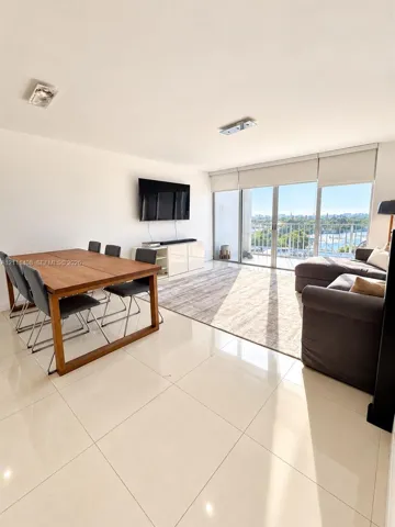 Large-format tile flooring, recessed ceiling lighting, and floor-to-ceiling glass sliding doors opening to a balcony with waterfront and city scenery