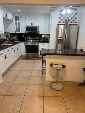 Kitchen featuring white shaker-style cabinetry, black stone countertops, stainless steel appliances, built-in wine storage, and ceramic tile flooring