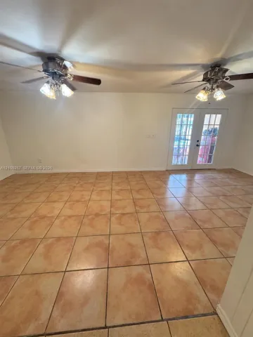 Large-format neutral tile flooring throughout, dual ceiling fans with multi-light fixtures, and white-paned French doors