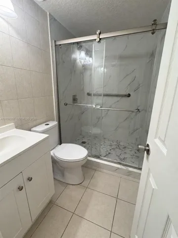 Bathroom featuring a white vanity with integrated basin, floor-to-ceiling tile, and a walk-in shower with sliding glass doors, stone-patterned wall surfacing, and metal hardware