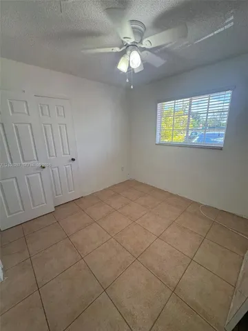 Interior space featuring ceramic tile flooring, a multi-pane window with horizontal blinds, double-door closet storage, and a ceiling-mounted fan with light fixture
