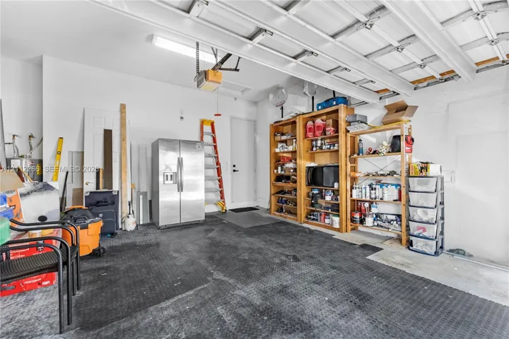 Garage space featuring high-reaching ceiling, overhead linear lighting, interior pedestrian door, and durable rubber flooring