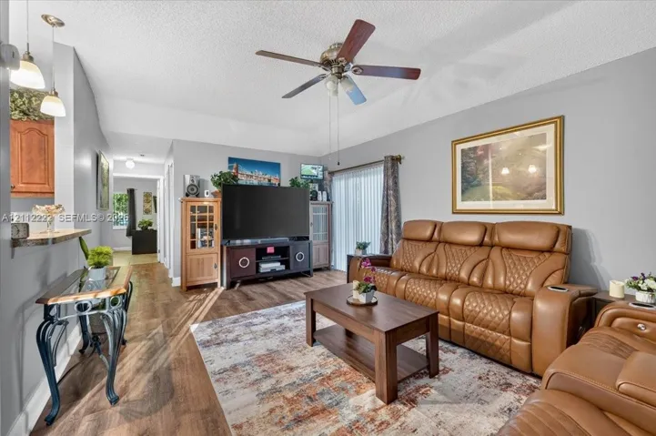 Living area featuring wood-finish flooring, vaulted ceilings, a ceiling fan, and sliding glass doors