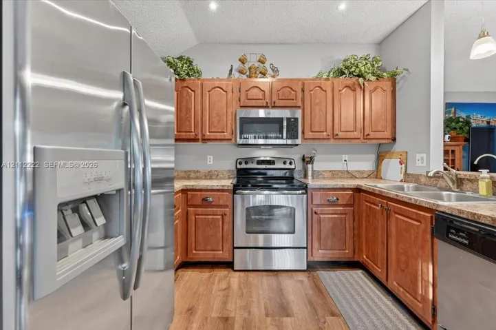 Kitchen featuring wood cabinetry, stainless steel appliances, neutral countertops, double-basin sink, and wood-finish flooring