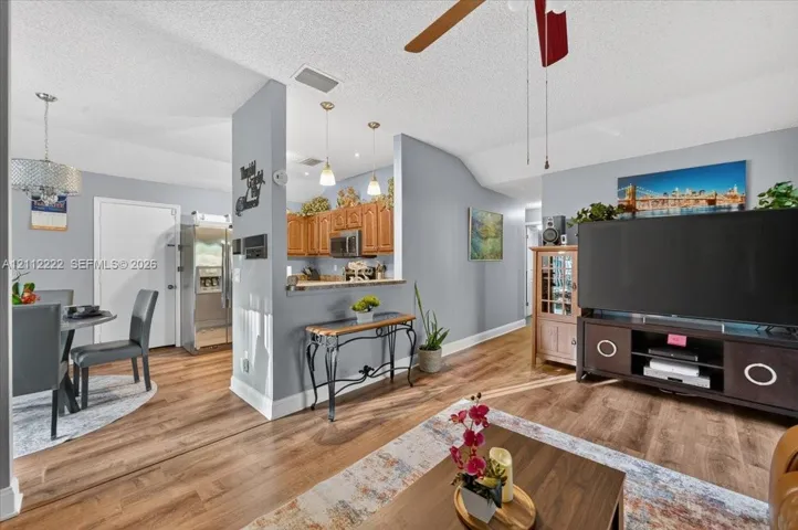Wood-finish flooring, pass-through breakfast bar, wood cabinetry, pendant lighting, and vaulted ceilings