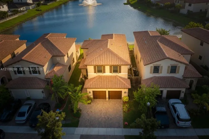 Two-story residence featuring a tile roof, two-car garage, and paver driveway, situated on a waterfront lot with an exterior water feature