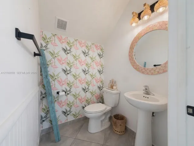Pedestal sink with polished chrome faucet, patterned wallcovering, tile flooring, and multi-light vanity fixture