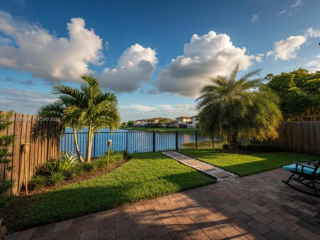 Waterfront backyard featuring a paver patio, a grass lawn, decorative stone walkway, and perimeter fencing