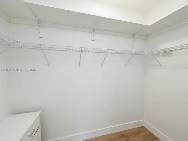 Walk-in storage space featuring built-in white shelving and wood-finish flooring