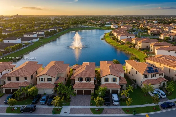 Aerial perspective of residential community featuring tiled roofs, paved driveways, a central water feature with a fountain, and integrated solar panel installations
