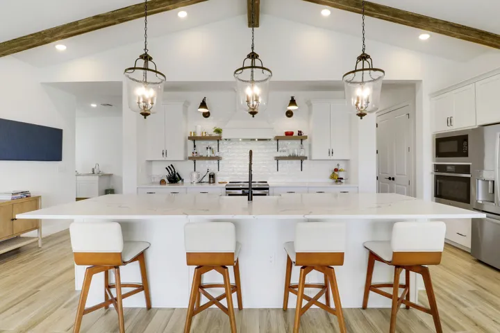 Kitchen featuring a central island with a stone-finish countertop, vaulted ceiling with exposed wood-finish like beams, white cabinetry, lantern-style pendant lighting, and subway tile backsplash