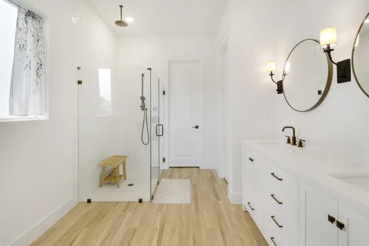 Double vanity with rectangular sinks, glass-enclosed walk-in shower featuring a rainfall showerhead, and wood like flooring
