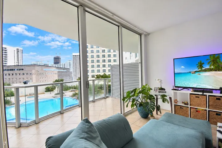Floor-to-ceiling glass sliding doors, expansive private balcony with glass railing, and ceramic tile flooring