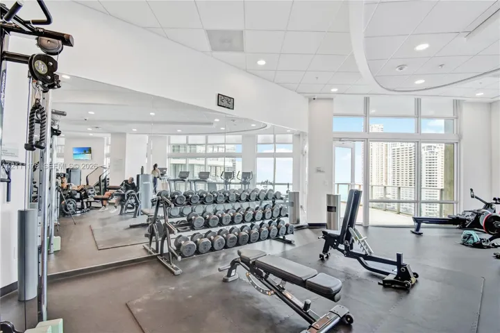 Fitness center featuring floor-to-ceiling windows, full-wall mirrors, recessed lighting, and rubberized flooring