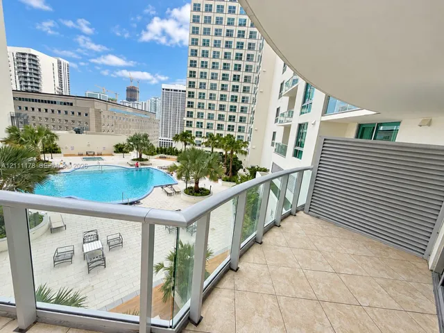 Covered balcony featuring tile flooring, metal railings with glass panels, and a privacy screen