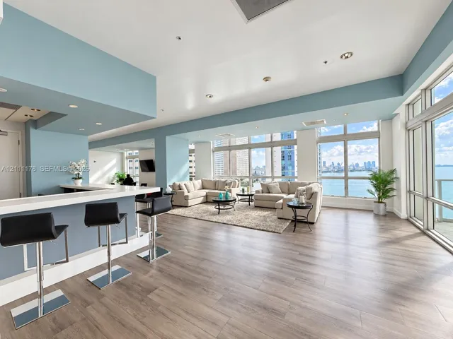 Open-concept living space featuring wood-finish flooring, floor-to-ceiling windows, a breakfast bar with stone-surface countertop, and recessed lighting