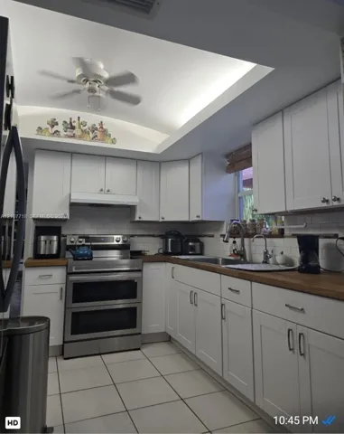 White cabinetry with shaker-style doors, wood-finish countertops, stainless steel dual-oven range, subway tile backsplash, and recessed tray ceiling with integrated lighting