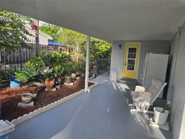 Covered concrete patio featuring a scalloped concrete landscape border, wood-mulch garden bed, and a exterior door with a multi-pane glass insert