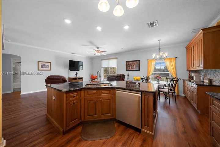 Kitchen featuring wood cabinetry, dark stone-surfaced countertops, a center island with an integrated stainless steel dishwasher, wood-finish flooring, and recessed ceiling lighting
