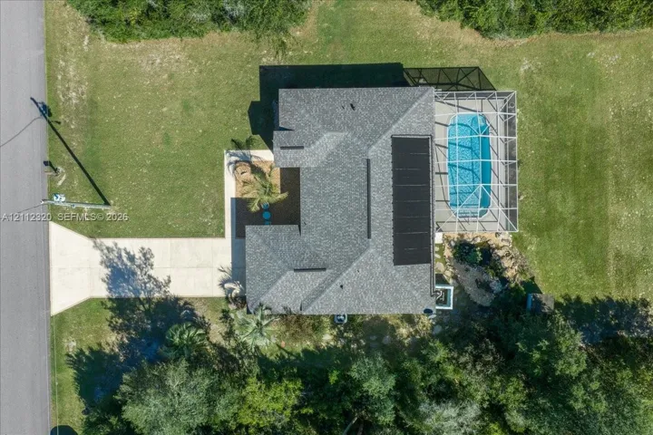 Aerial perspective featuring an asphalt shingle roof, roof-mounted solar panels, an in-ground pool, a screened-in pool enclosure, and a concrete driveway