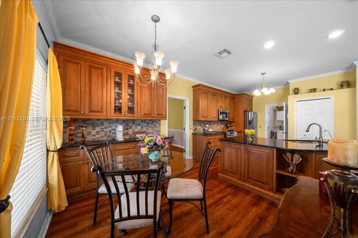 Kitchen featuring medium-tone wood cabinetry, granite countertops, stone-tile backsplash, wood-finish flooring, and a multi-tiered chandelier
