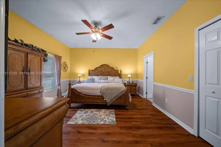 Room featuring wood-finish flooring, two-tone wall paint with chair rail molding, ceiling fan with integrated lighting, and a multi-panel closet door