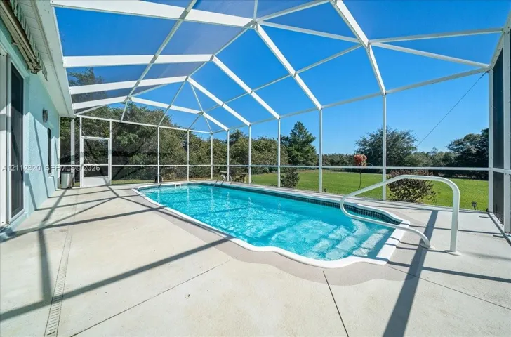 Screened-in patio featuring a swimming pool, concrete deck, and pool entry handrail