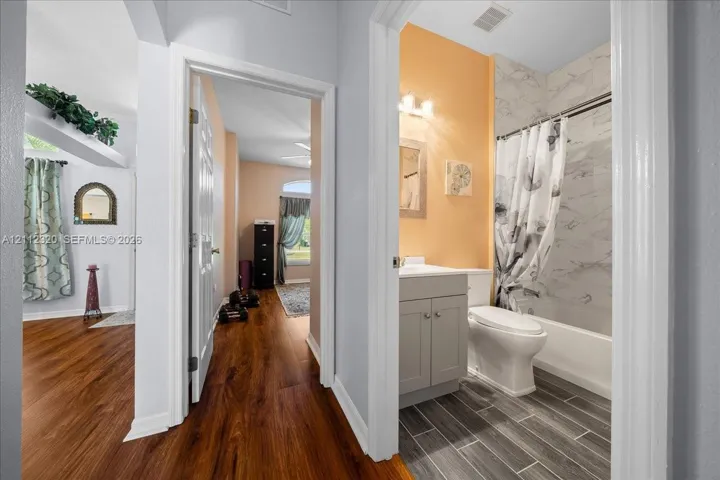 Bathroom featuring a stone-finish tub surround, wood-finish floor planks, and a shaker-style vanity with a solid-surface countertop
