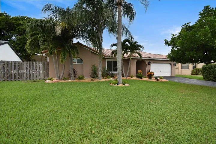 Single-story stucco exterior featuring a tiled roof, multi-car garage, manicured lawn, and mature palm landscaping