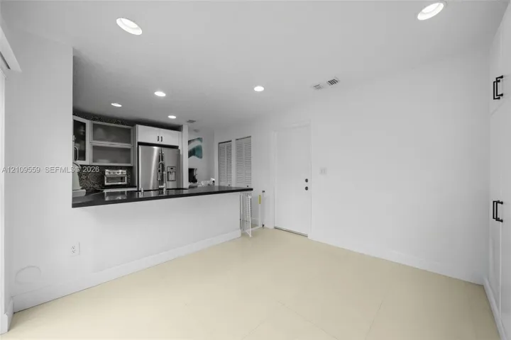 Kitchen featuring a breakfast bar with dark countertop, stainless steel refrigerator, recessed lighting, tile flooring, and floor-to-ceiling built-in cabinetry