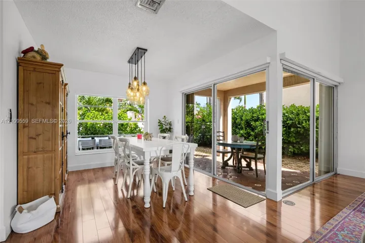 Wood-finish flooring, multi-pane window, suspended linear light fixture, and floor-to-ceiling glass sliding doors opening to a covered patio
