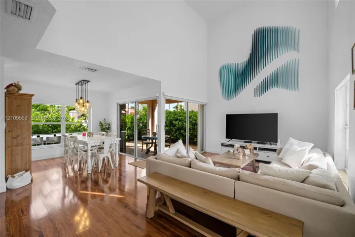 High-ceiling living area featuring wood-finish flooring, floor-to-ceiling glass sliding doors, and multi-pendant dining room lighting