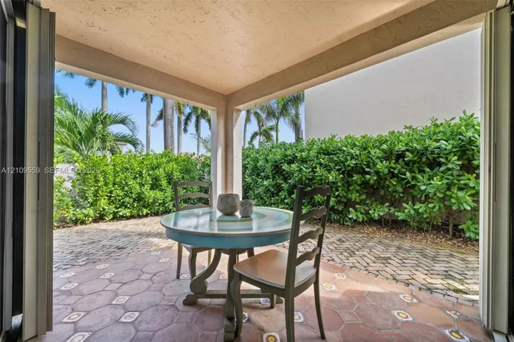 Covered patio featuring decorative tile flooring, brick paver hardscaping, and perimeter shrubbery