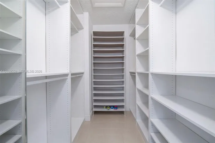 Walk-in closet featuring extensive built-in white shelving, multiple hanging rods, and dedicated floor-to-ceiling shoe storage