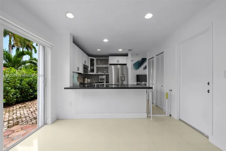 Kitchen featuring white shaker-style cabinetry, dark stone countertops, stainless steel appliances, tile flooring, and sliding glass doors