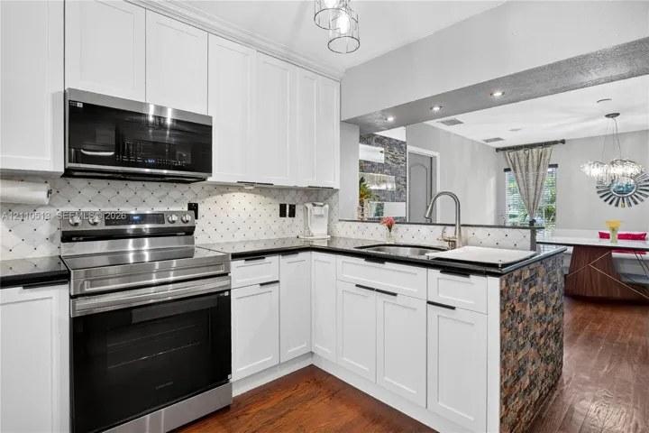 Modern kitchen featuring white shaker cabinetry, stainless steel appliances including a double wall oven, black quartz countertops, a decorative tile backsplash, and a large island with wood-tone base